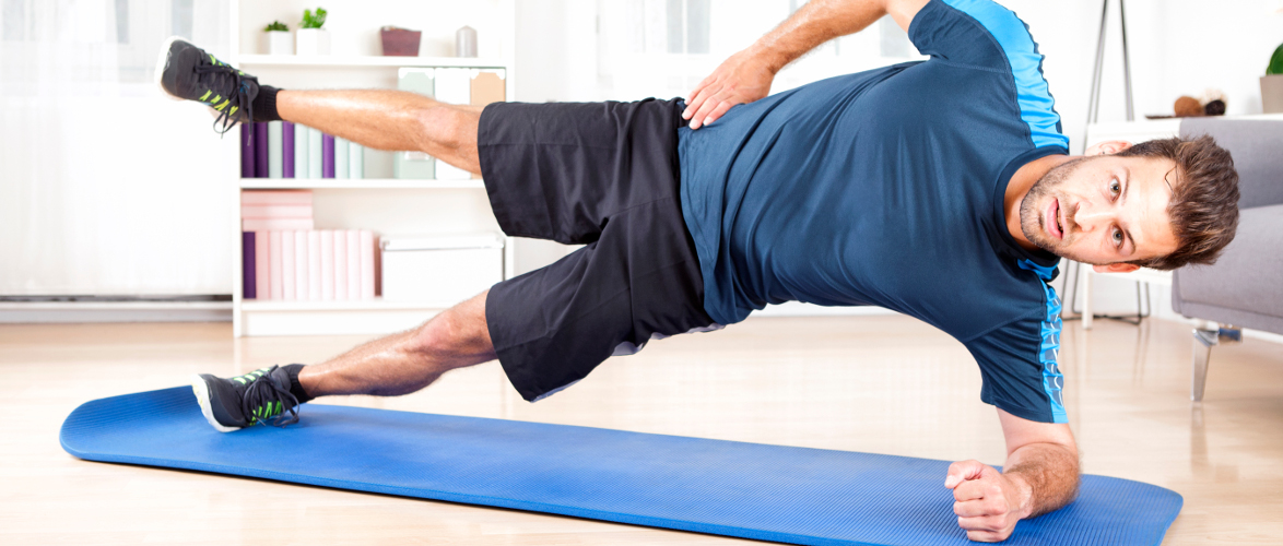 Full Length Shot of a Handsome Athletic Man Doing Side Plank Exercise with One Leg Raised, Looking at the Camera.