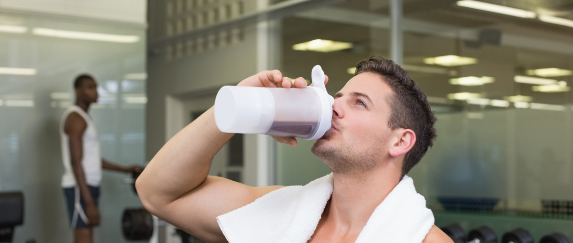 Shirtless bodybuilder drinking protein drink sitting on bench at the gym